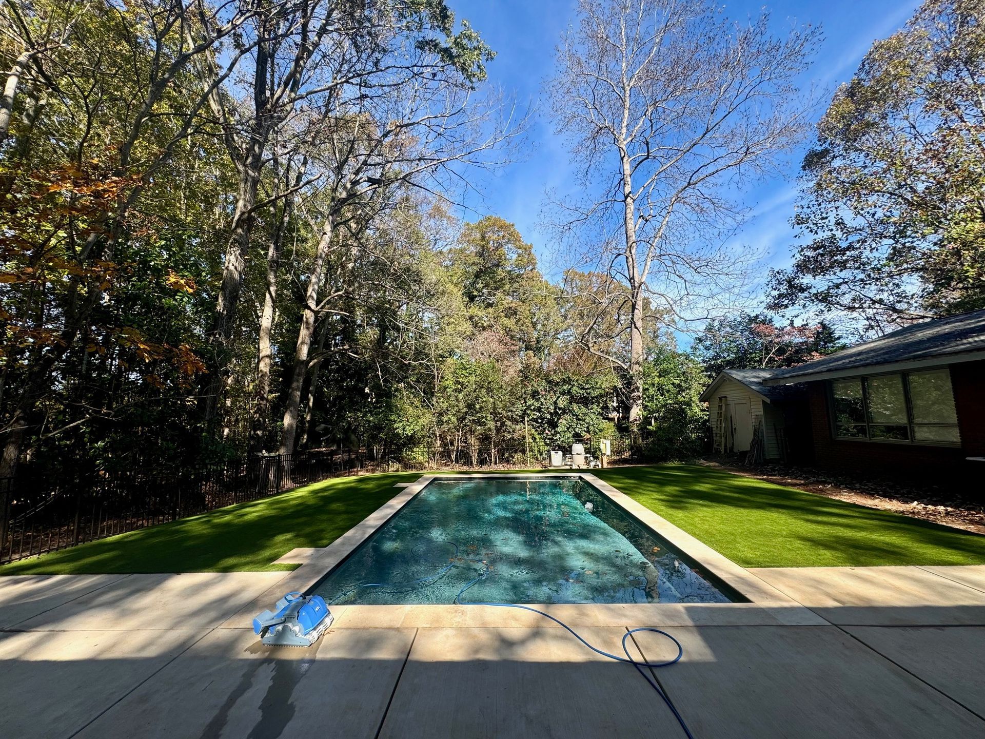 A large swimming pool in the backyard of a house surrounded by trees.