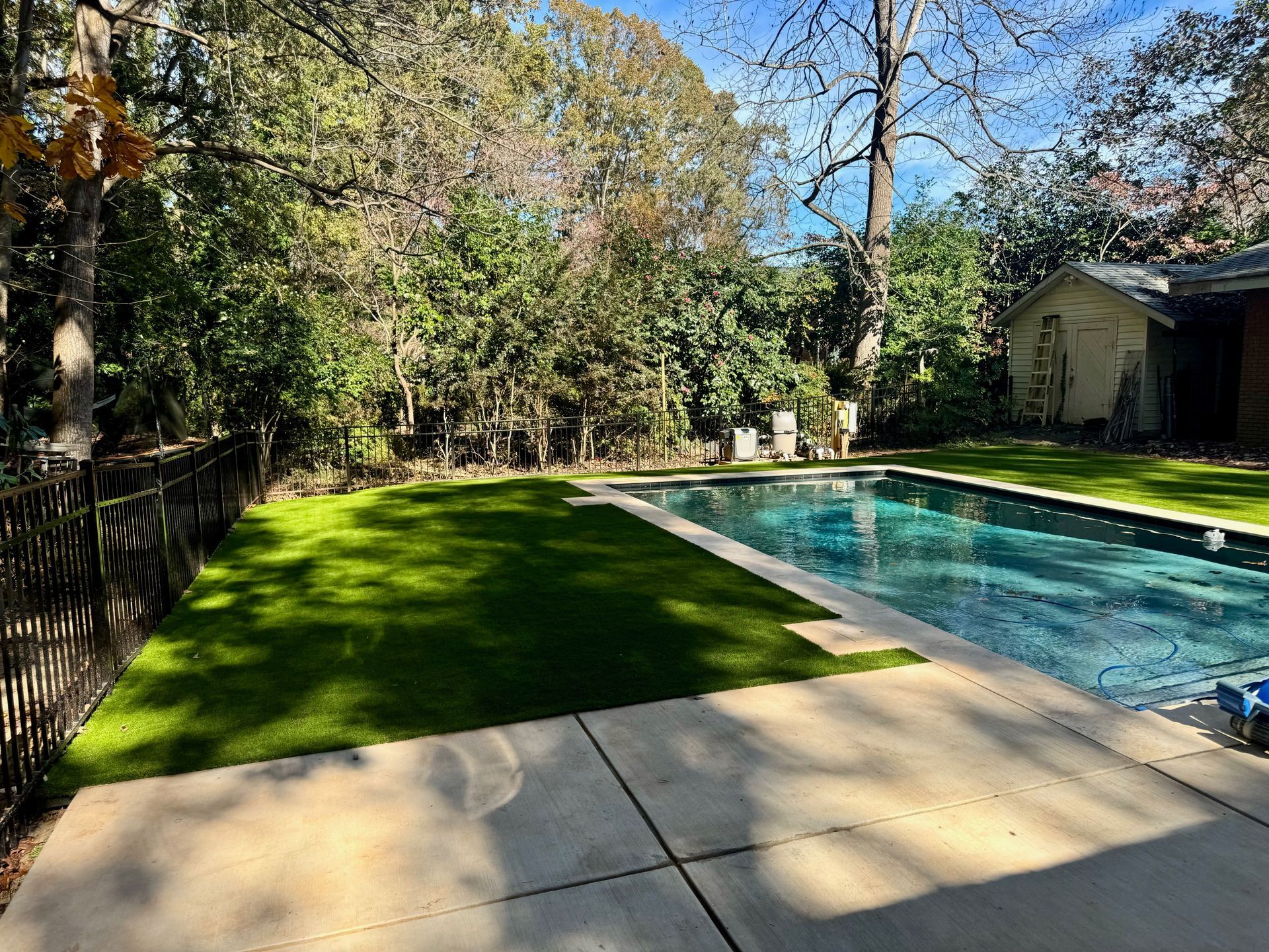 A large swimming pool in the backyard of a house surrounded by trees.