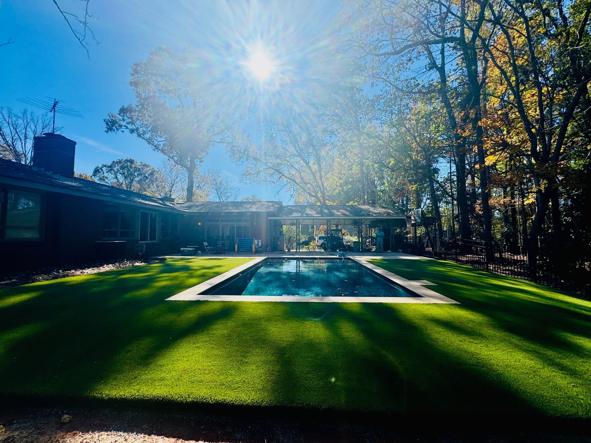 There is a large swimming pool in the backyard of a house surrounded by trees.