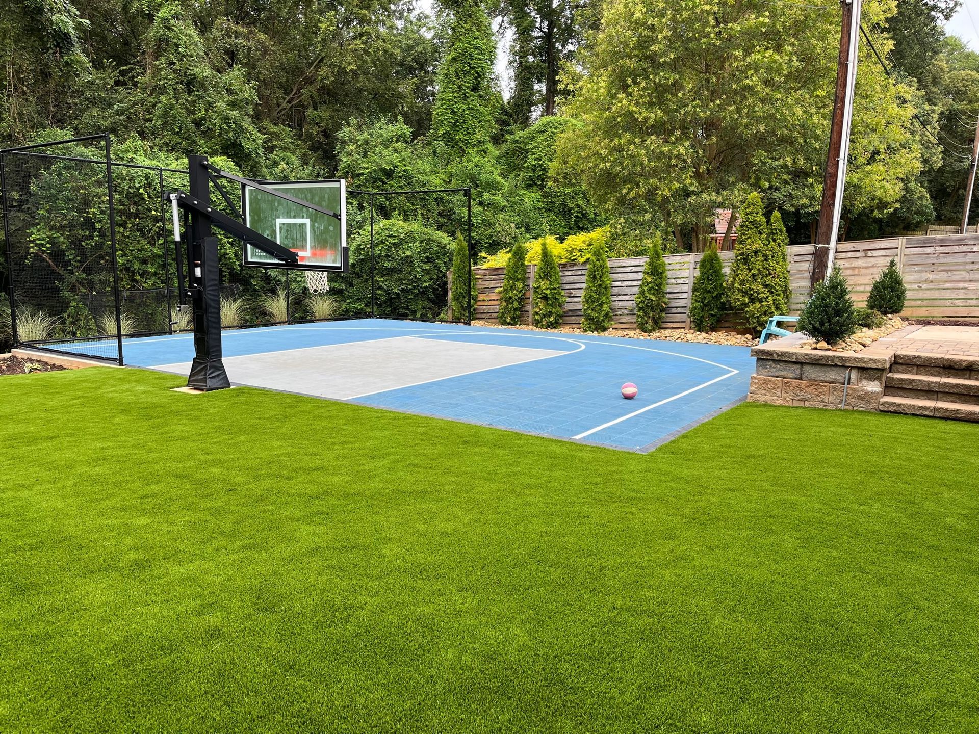 There is a basketball court in the backyard with a basketball hoop.
