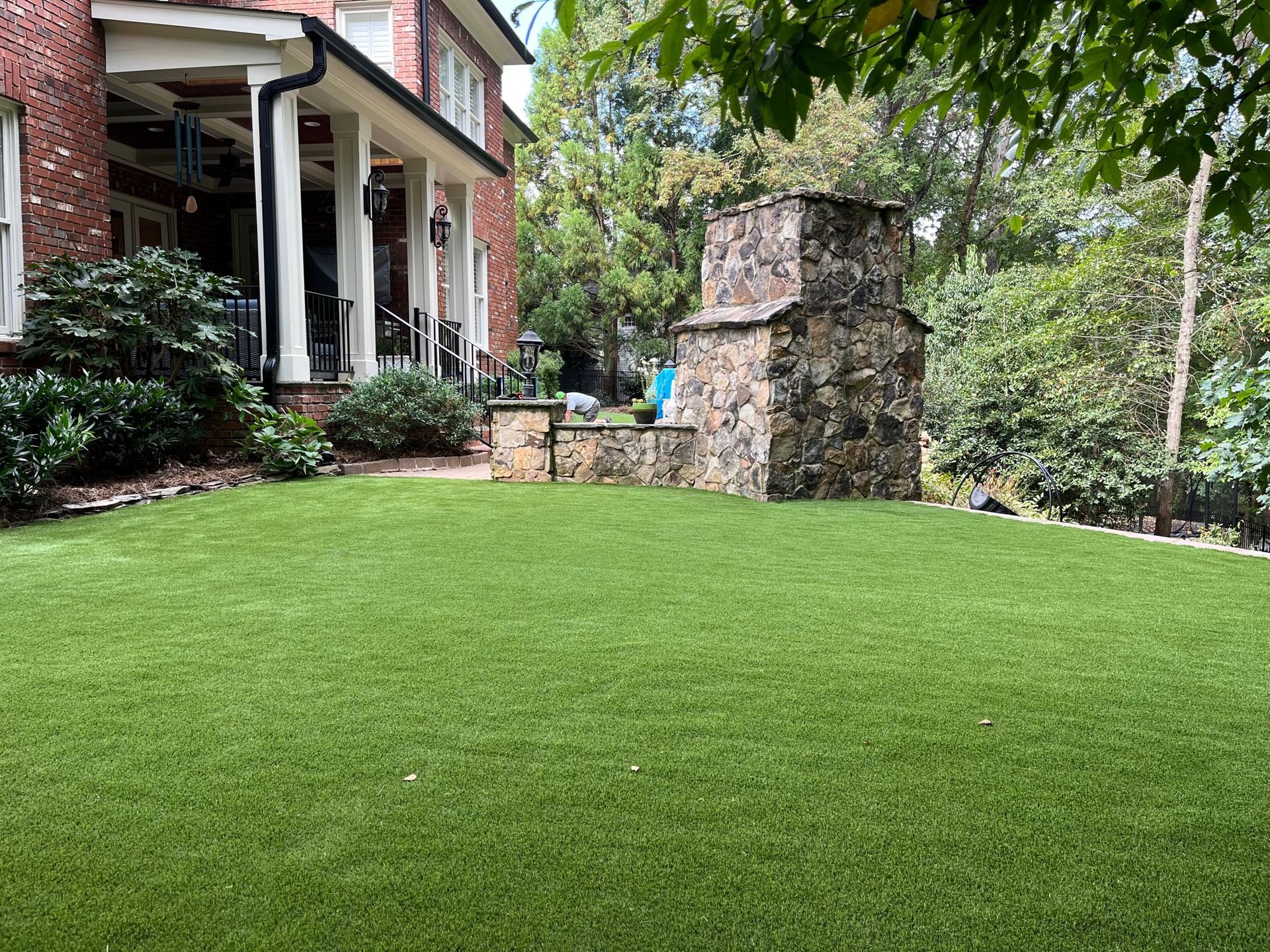 A large lawn in front of a brick house with a stone fireplace.