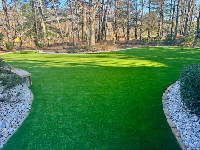 A lush green lawn with trees in the background and a path leading to it.