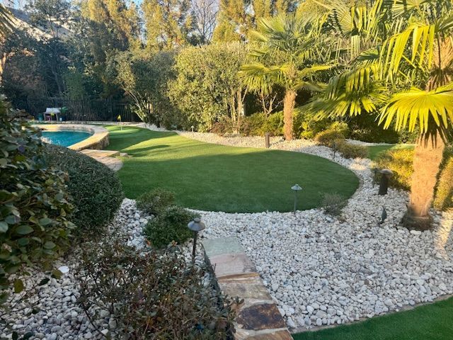 A lush green garden with a swimming pool in the background.