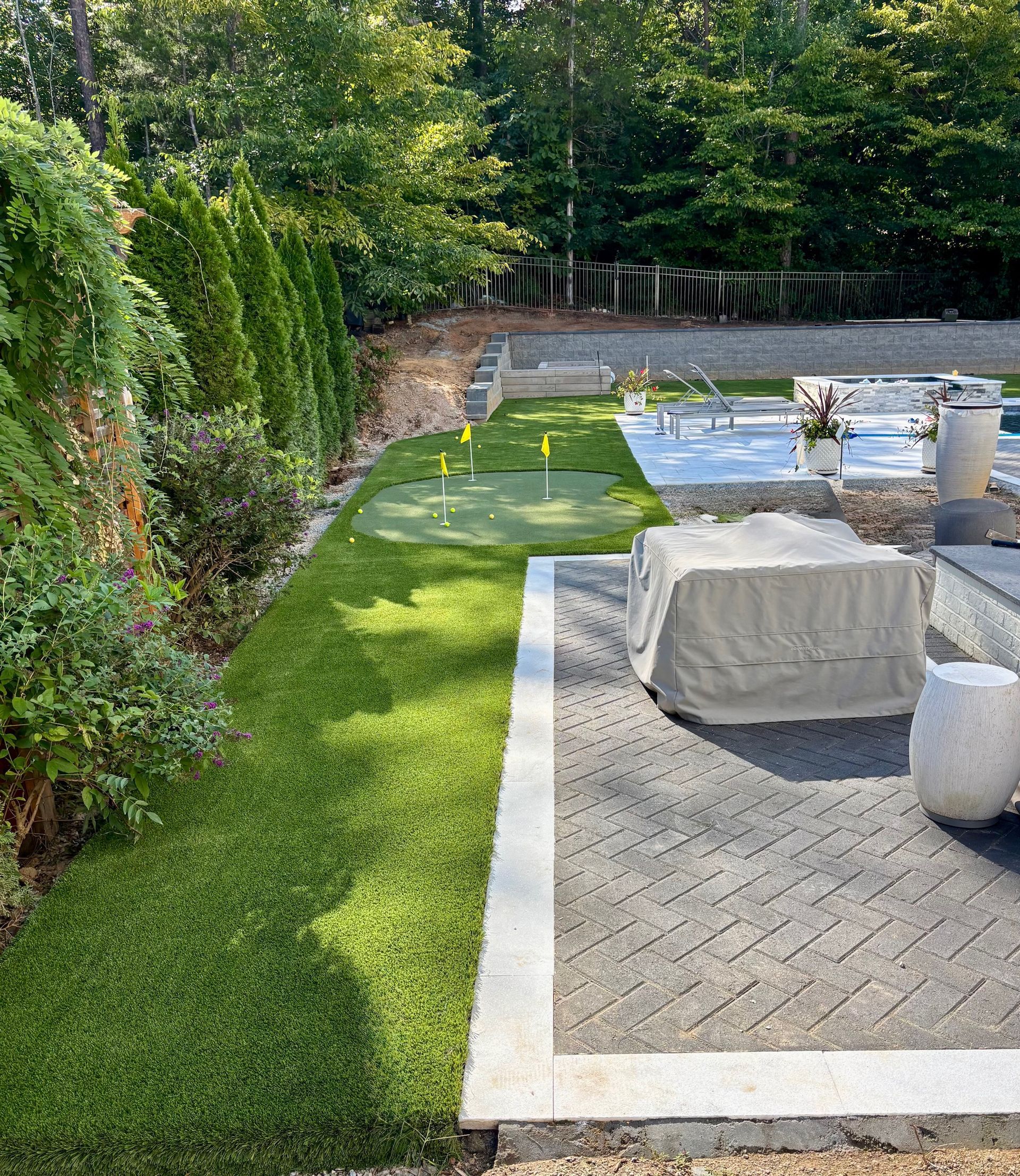 Backyard with putting green, pavers, seating area, and tall green hedges.