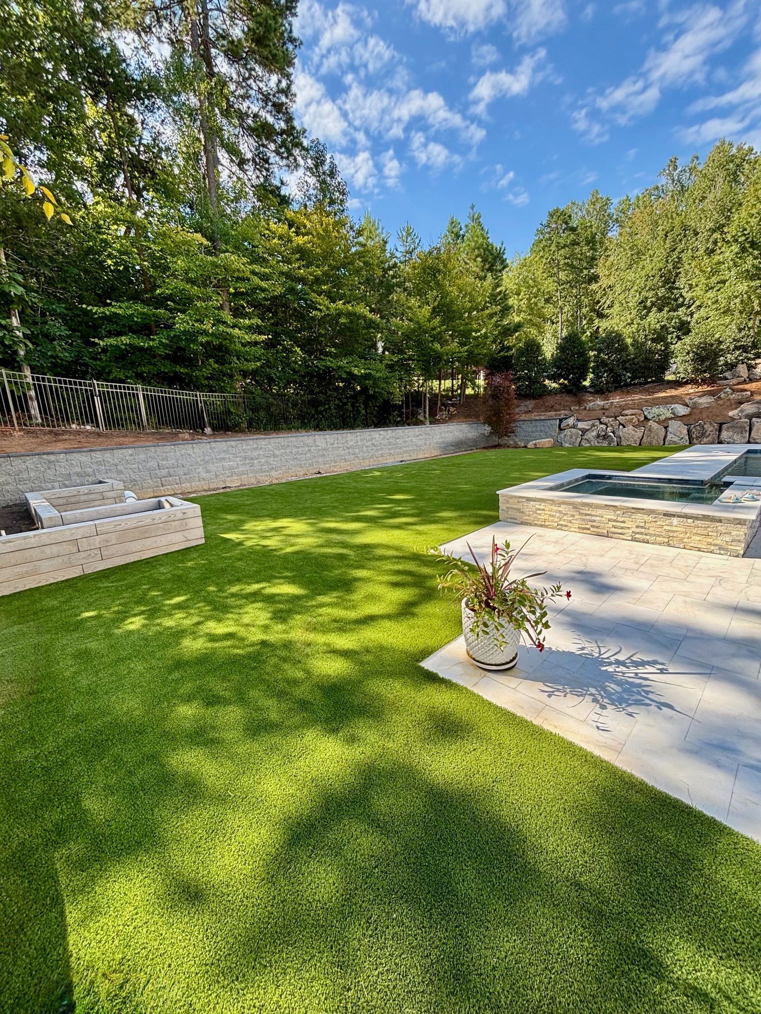Backyard with green grass, stone patio, and a small pool under a blue sky.
