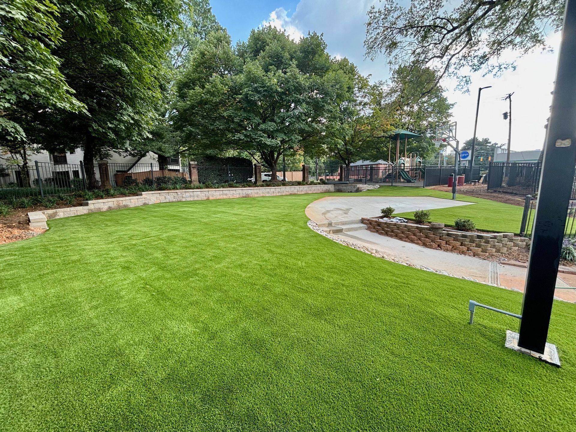 Green park with manicured grass, curved path, and trees under a cloudy sky.