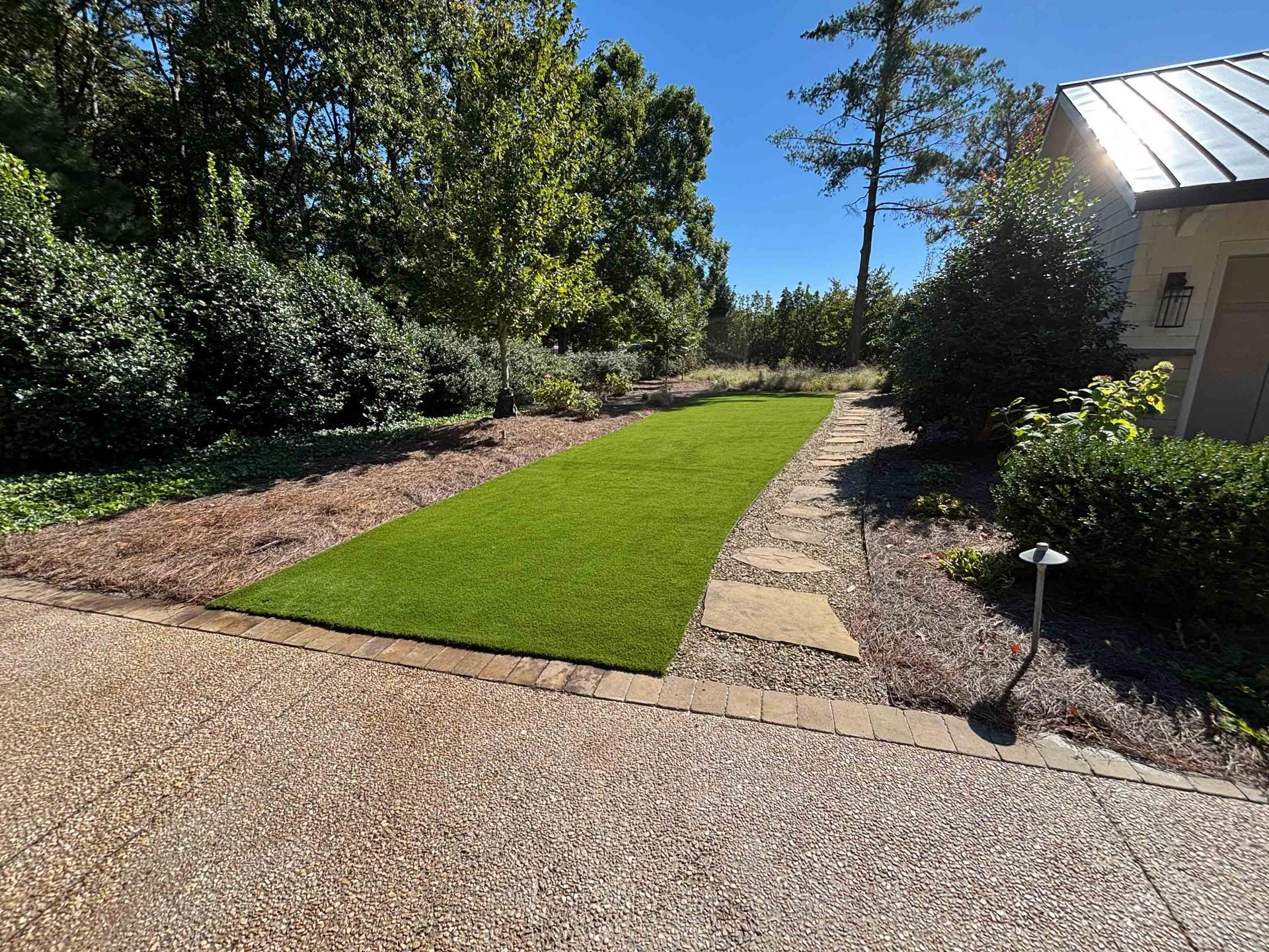 A patch of green artificial grass with stone path beside a driveway.