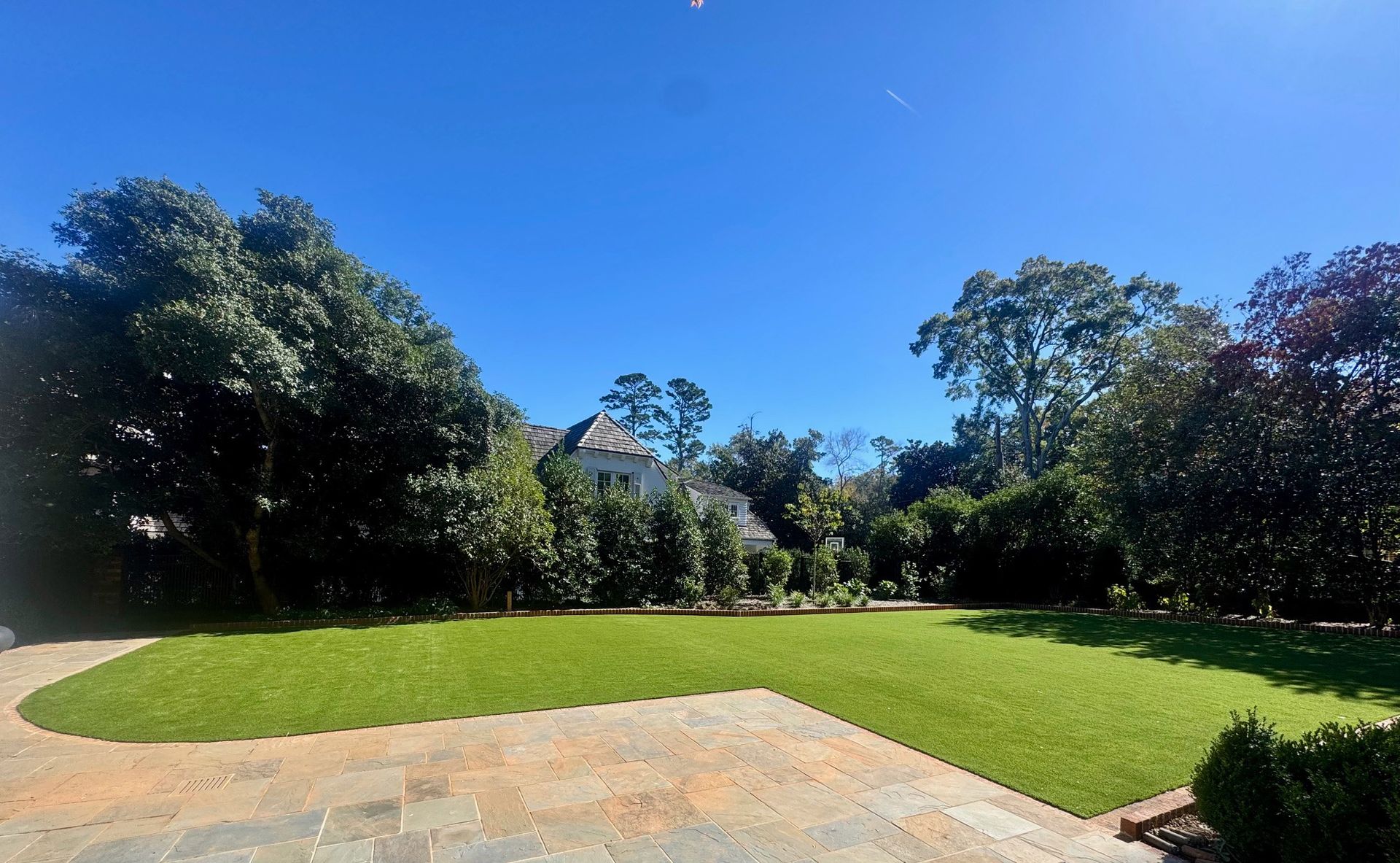 Lush green lawn framed by trees, leading to a white house under a bright blue sky.