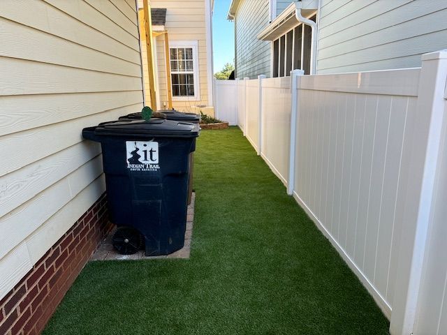 A black garbage can with the word sit on it sits next to a white fence