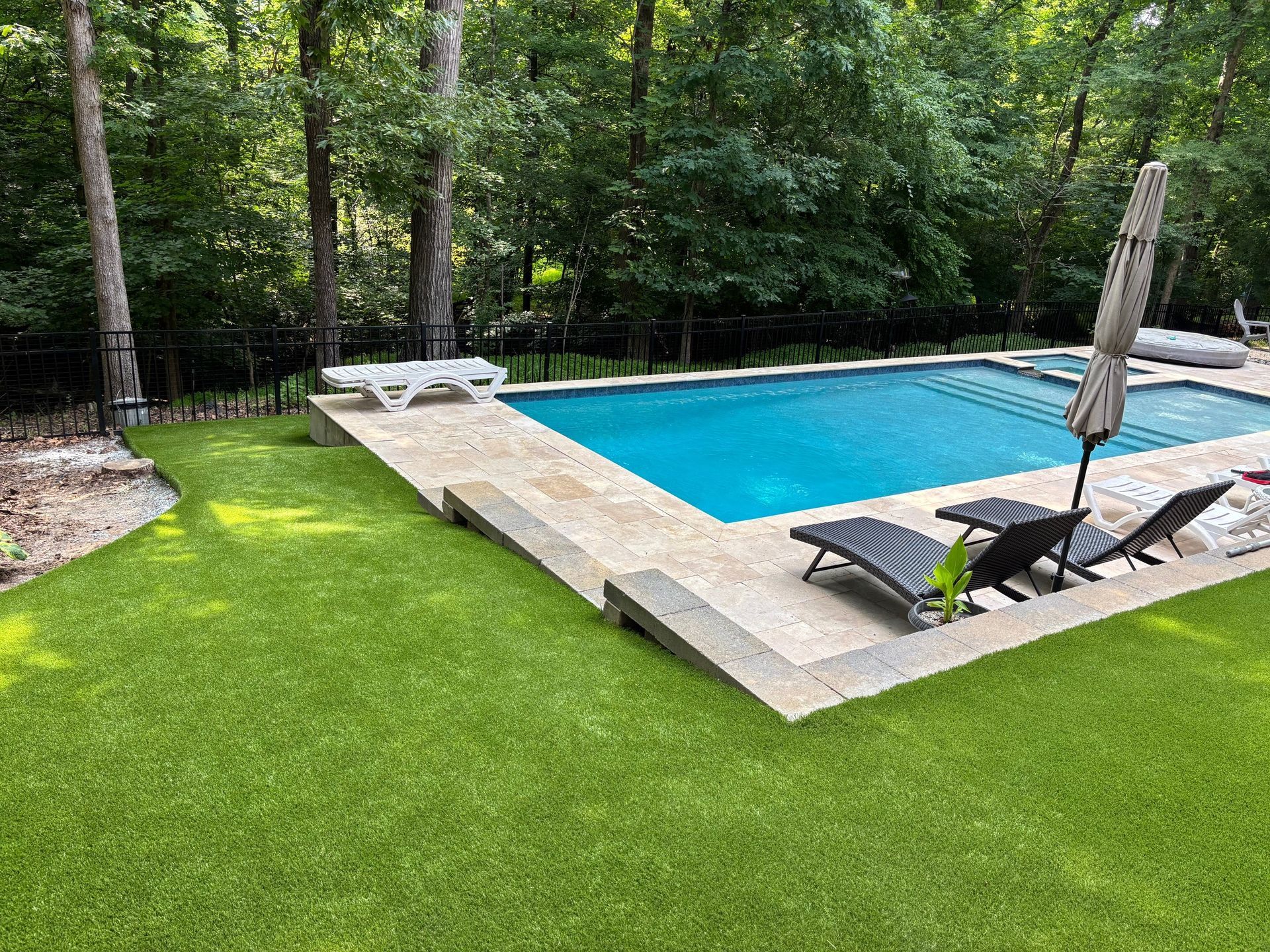 A large swimming pool surrounded by chairs and umbrellas in a backyard.