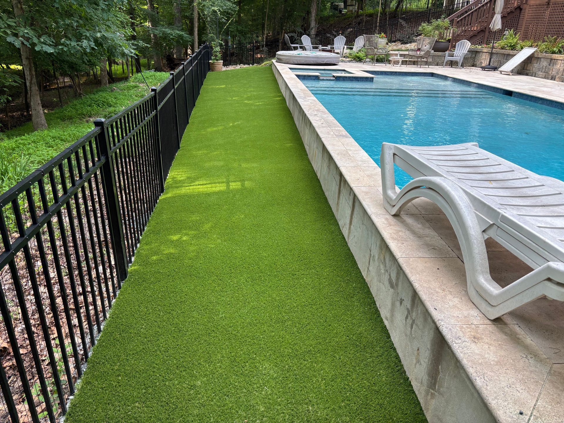 A swimming pool surrounded by a fence and a lush green lawn.