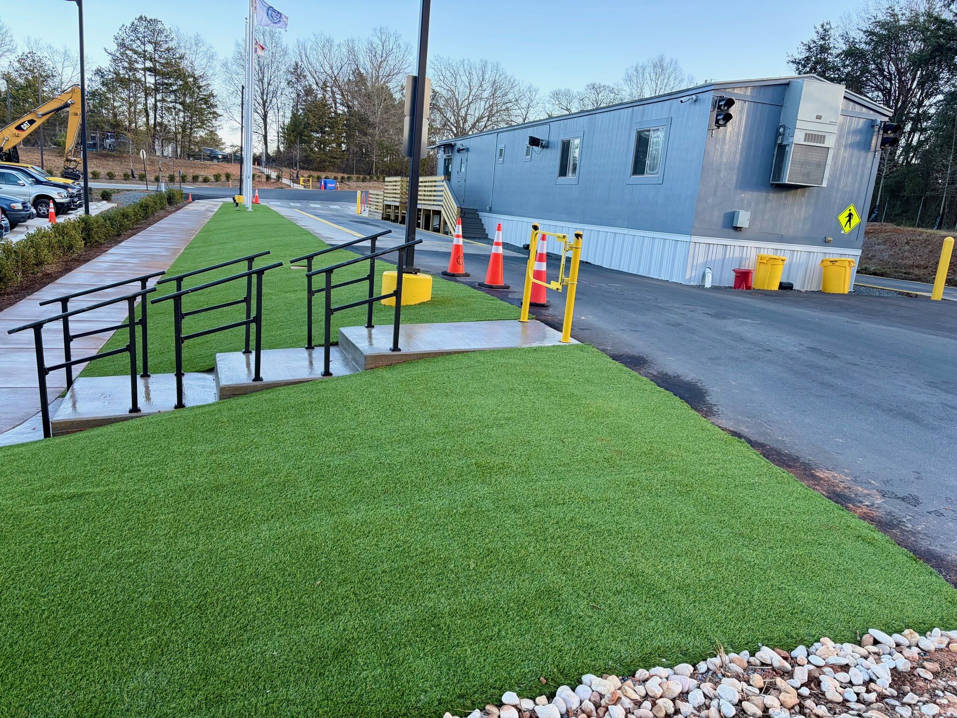 A large, gray utility structure being transported on a road. Artificial green grass and a wheelchair ramp are in the foreground.