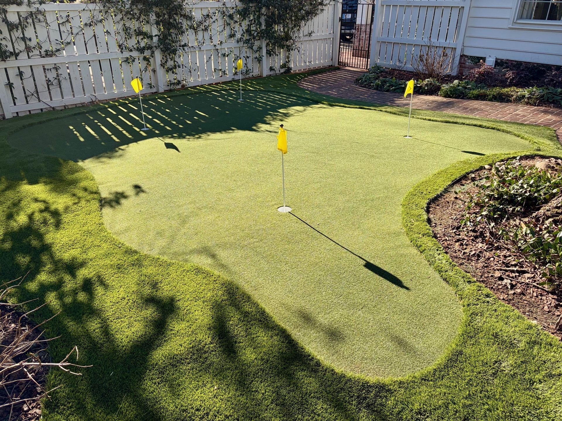 Artificial turf putting green in a backyard, with three yellow flagsticks.