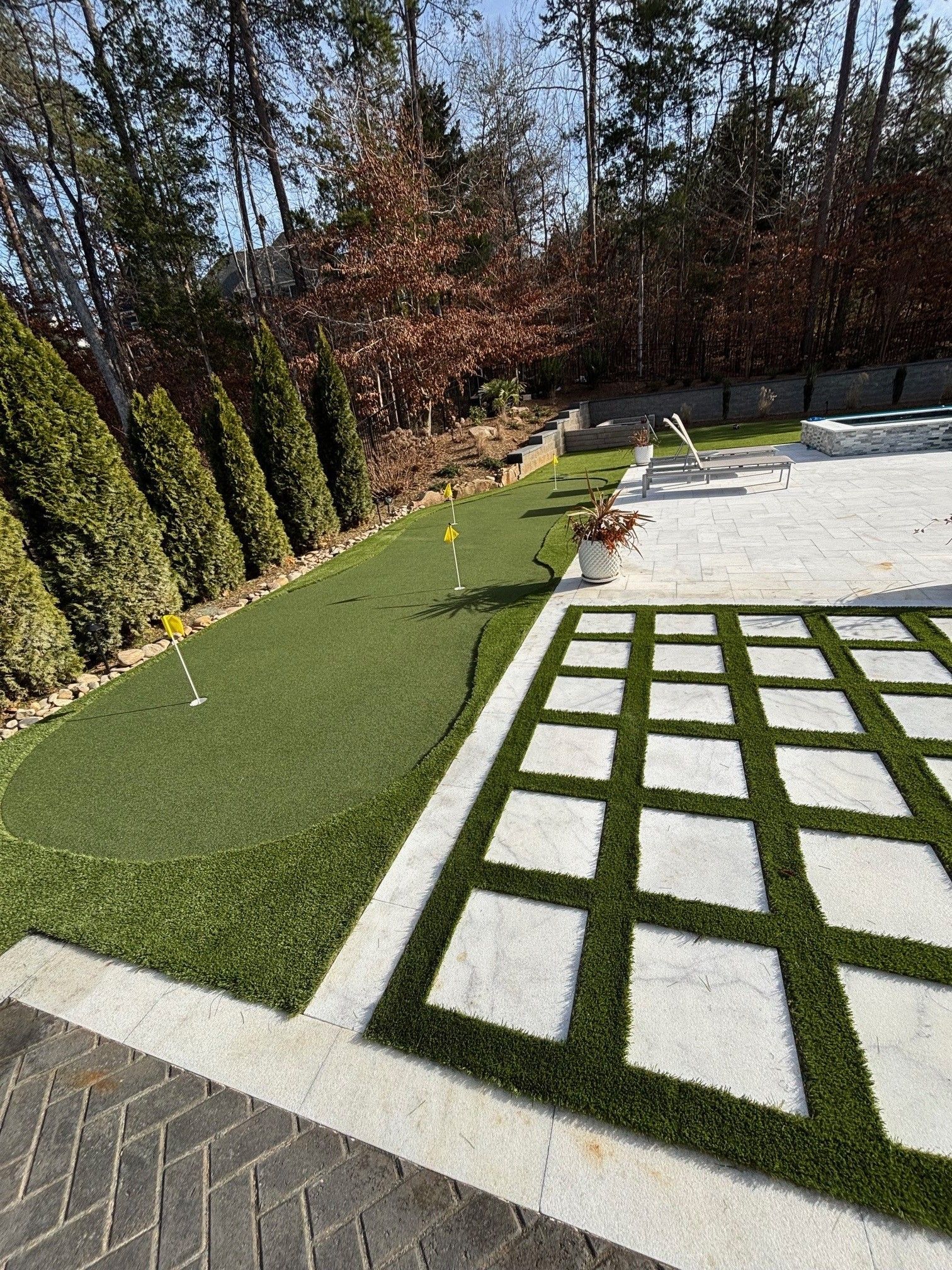Artificial turf putting green next to a stone patio with decorative square grass inserts.