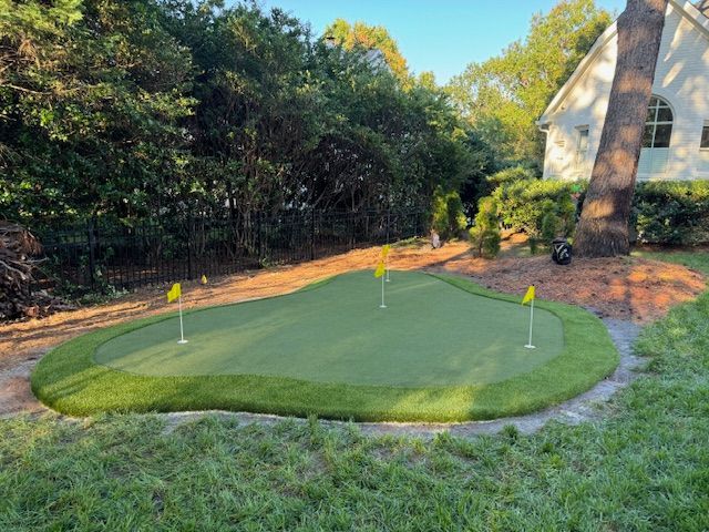 A golf course in a backyard with a house in the background.