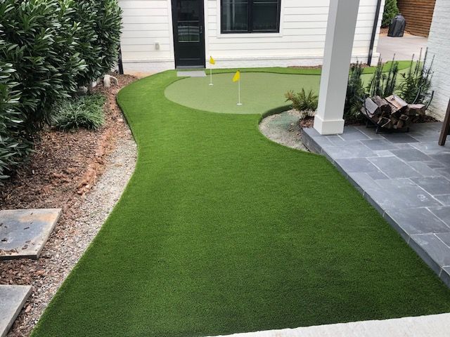 There is a putting green in the backyard of a house.