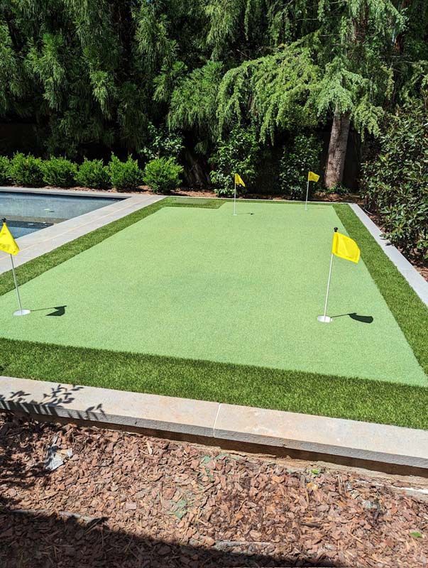 A putting green with yellow flags and a pool in the background.