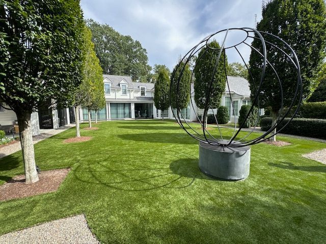 A large sculpture is in the middle of a lush green lawn in front of a house.