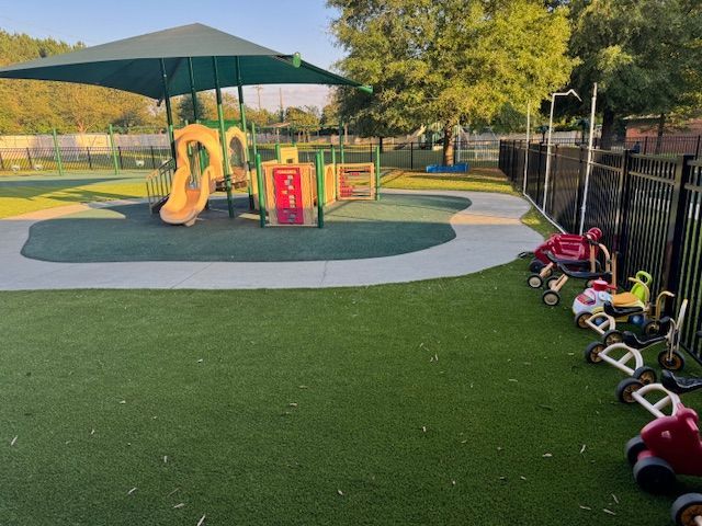 A playground with a green umbrella and a lot of toys on the grass.