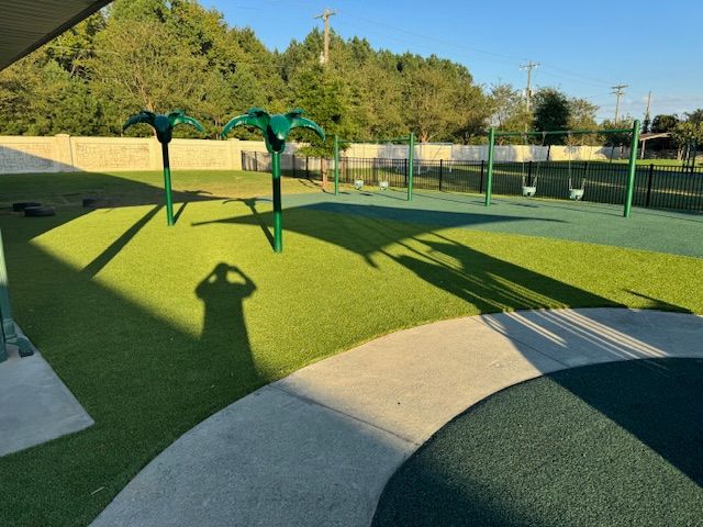 A shadow of a person is cast on the grass in a playground