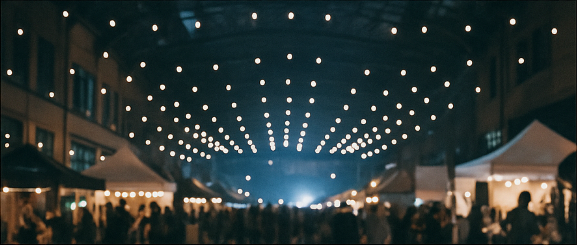 A crowd of people are gathered under a ceiling of lights at night.