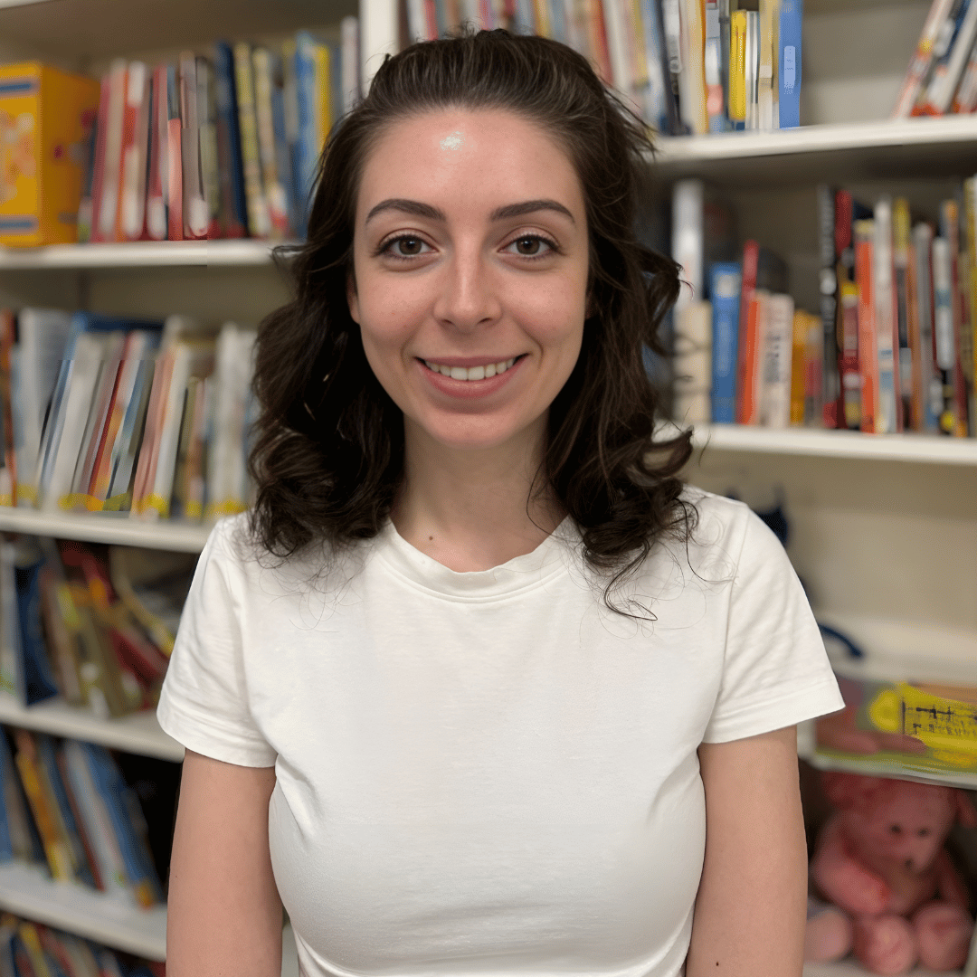 A woman in a white shirt is smiling in front of a bookshelf.