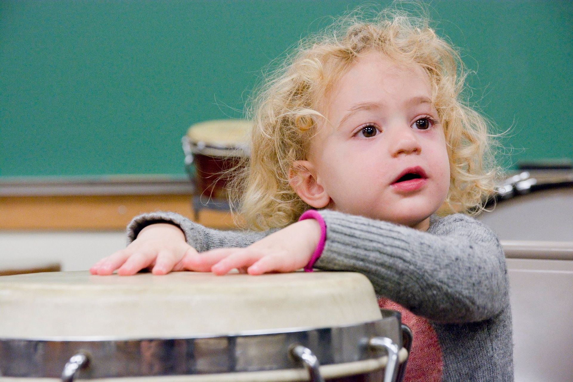 A little girl is leaning on a drum in a classroom.