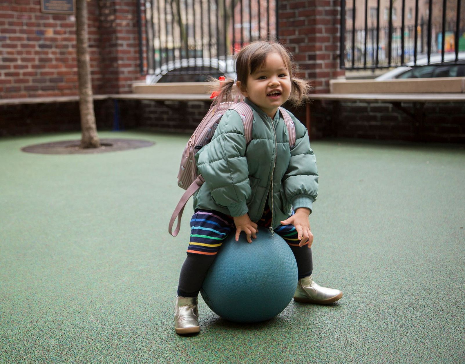 A little girl is sitting on a blue ball in a playground.