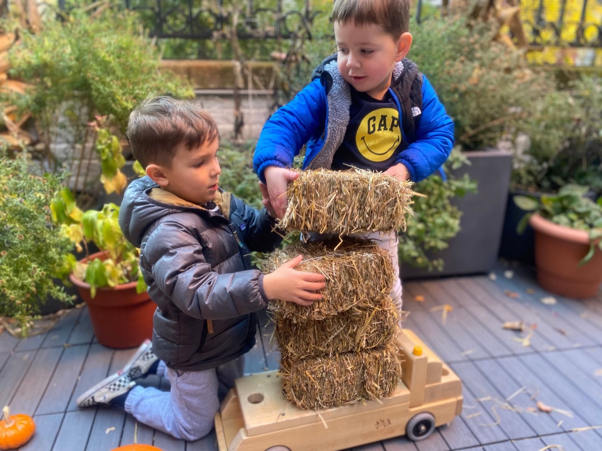 Two young boys are playing with hay bales on a wooden toy truck.