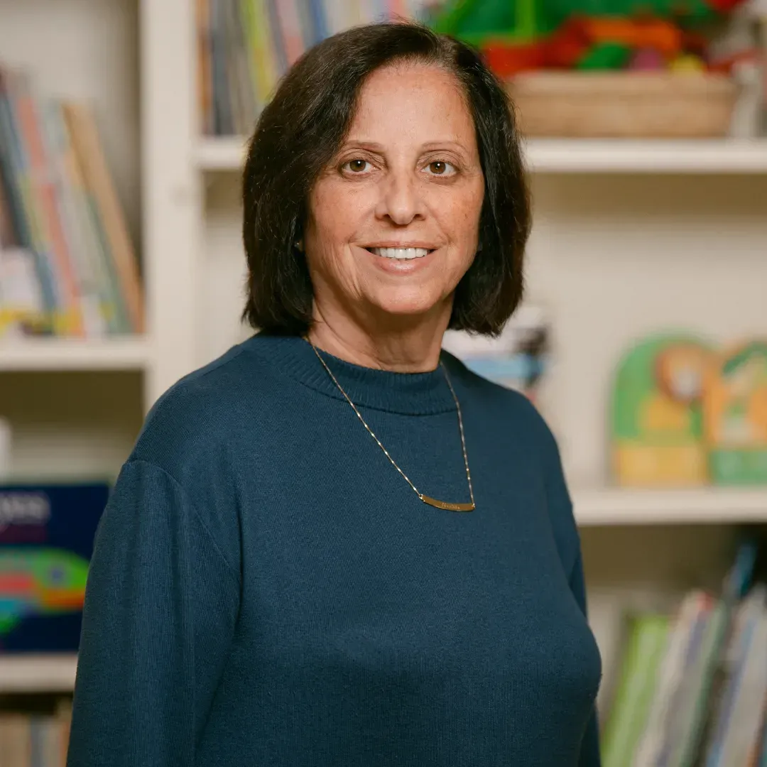 A woman in a blue sweater is standing in front of a bookshelf.