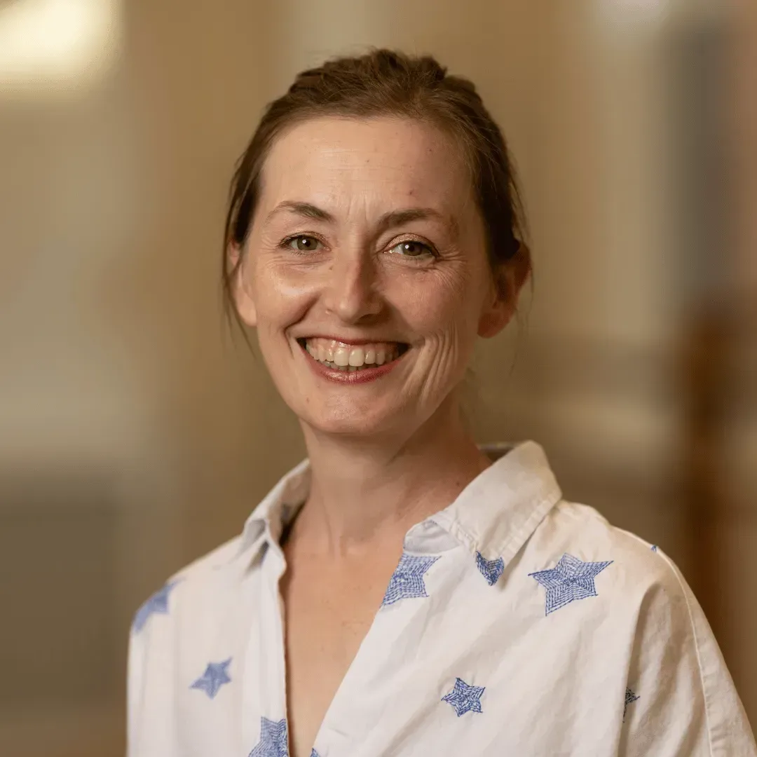 A woman in a white shirt with blue stars on it is smiling for the camera.