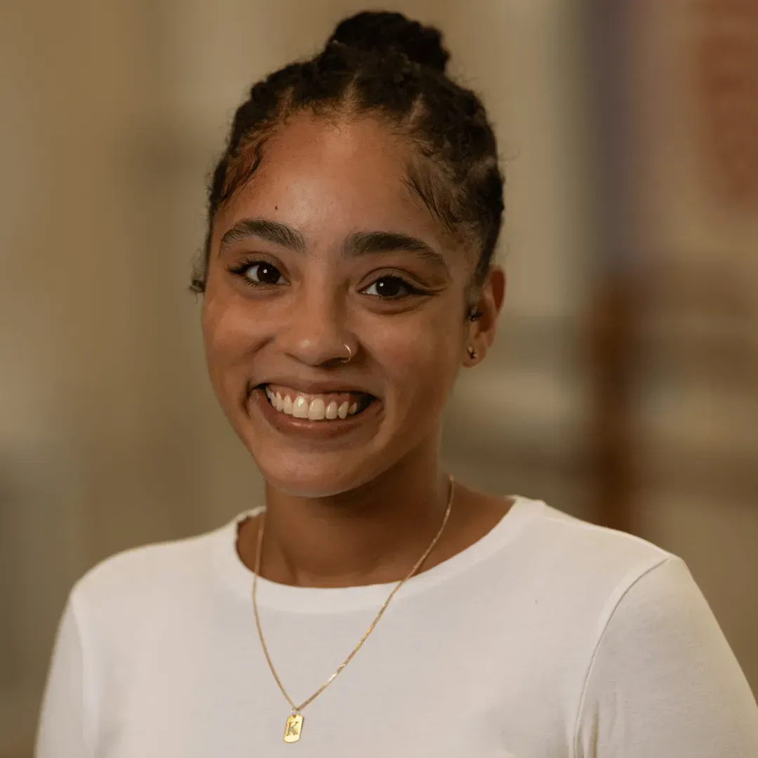 A young woman wearing a white shirt and a gold necklace is smiling for the camera.