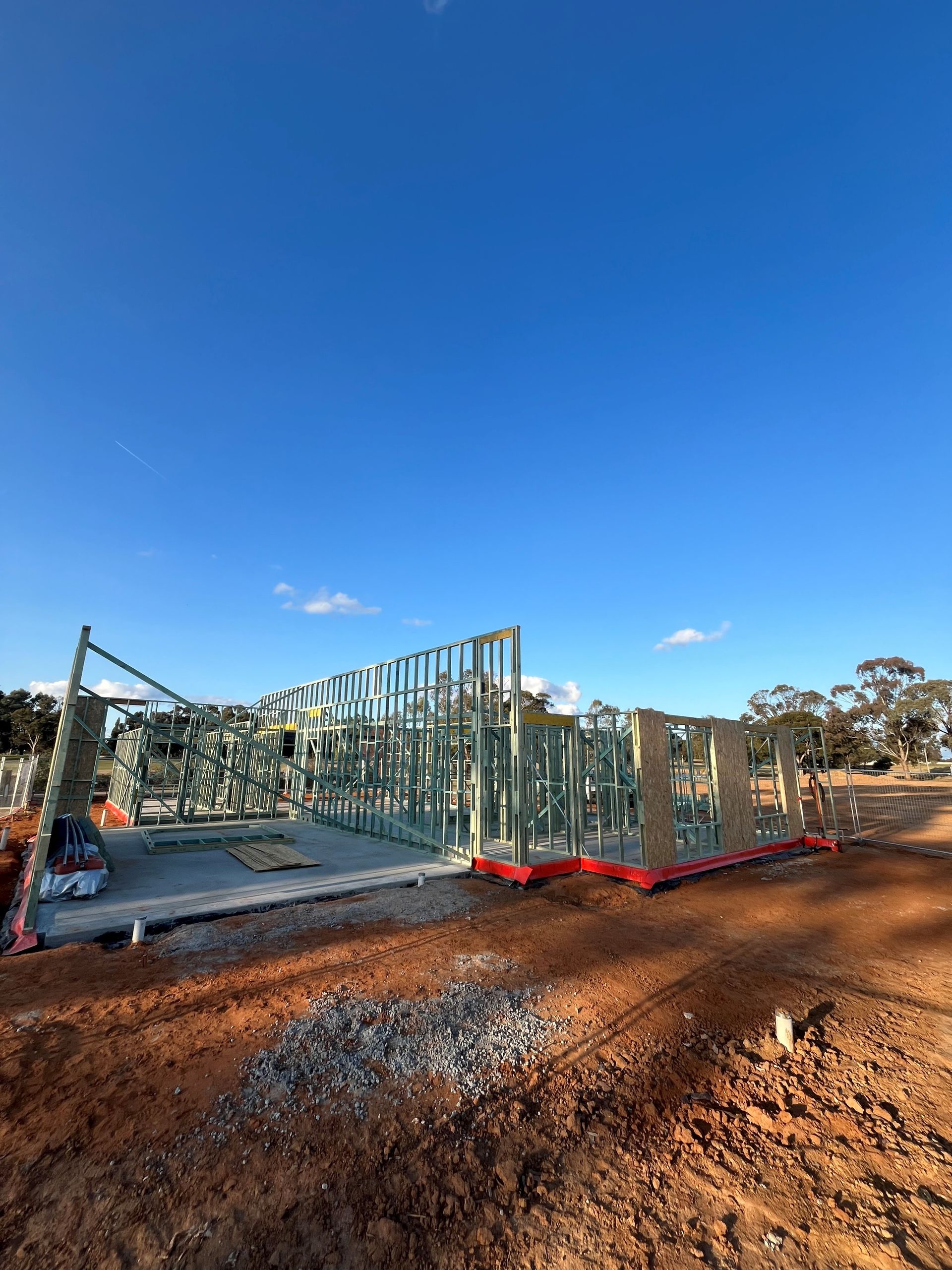 Framing of a building under construction against a blue sky. The structure is made of wooden beams on a dirt lot.