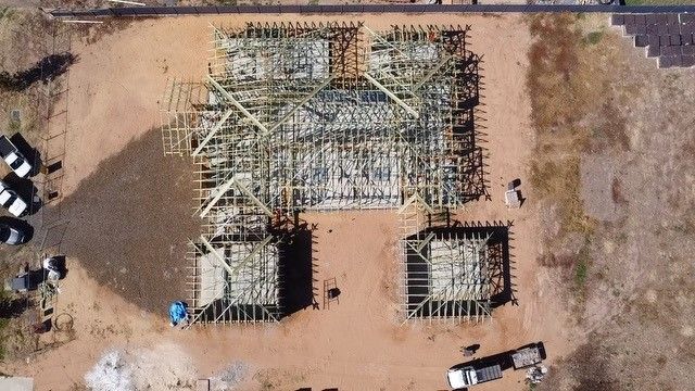 Aerial view of a building under construction, showing wooden framework on a dirt lot with vehicles nearby.