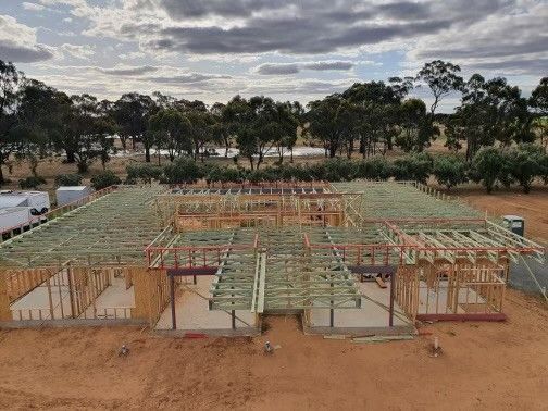 Construction site of a house in progress, wooden frame visible against a backdrop of trees and a cloudy sky.