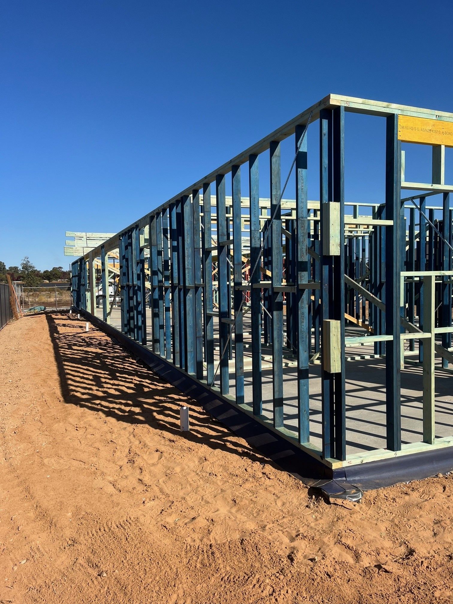 Construction site with a blue metal frame structure on a brown dirt lot, under a clear blue sky.