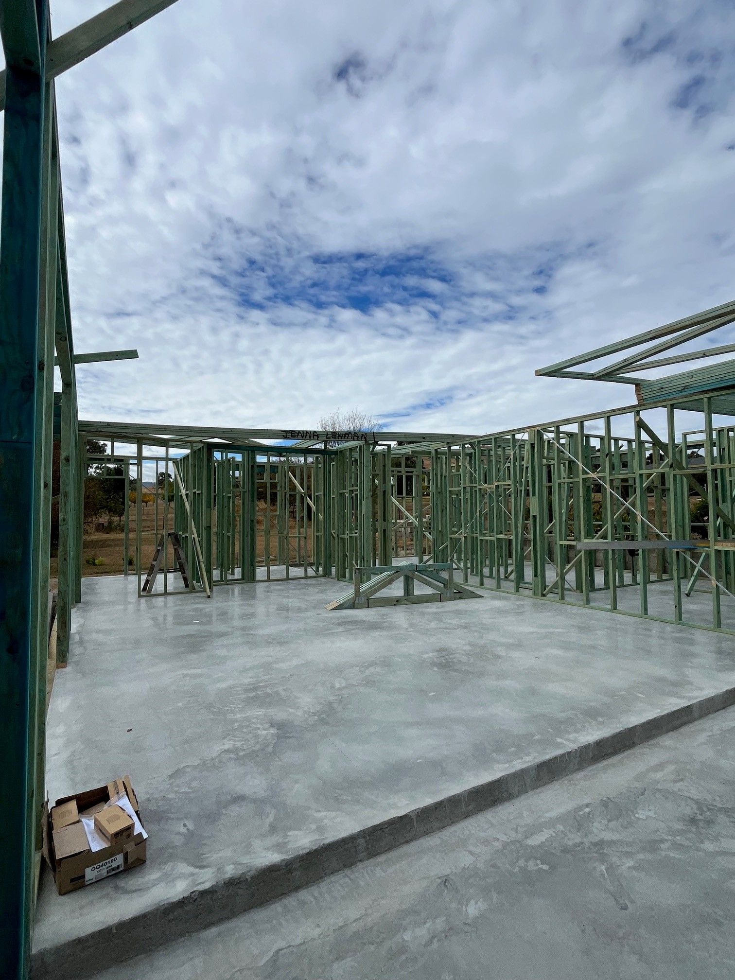 Interior view of a house under construction. Wooden frame walls and ceiling on a concrete slab, with a cloudy sky visible.