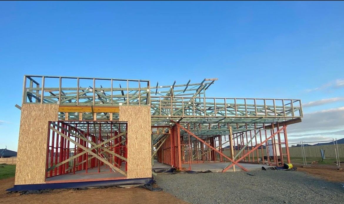 Construction site of a house, with wooden framing and a partially completed roof against a blue sky.