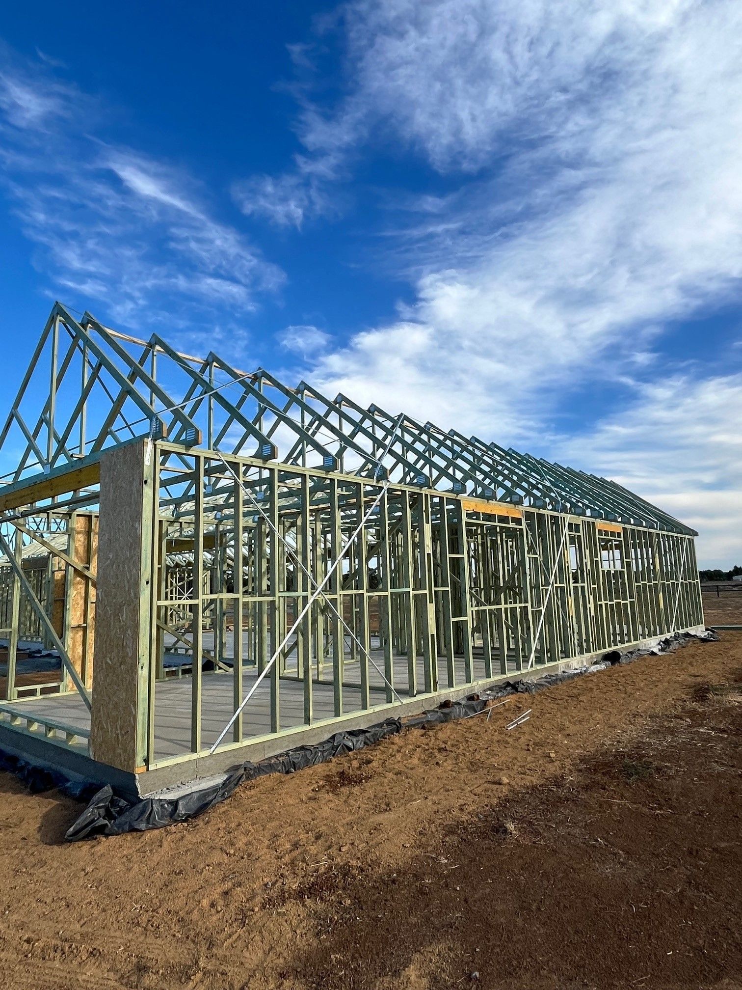 Framing of a building under construction, with exposed wooden beams against a blue sky with wispy clouds.