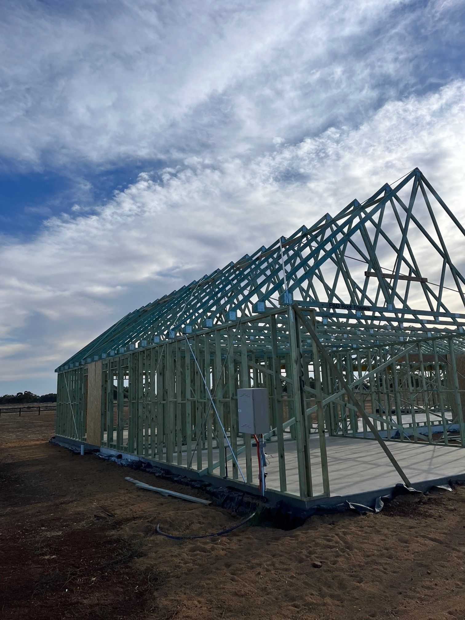 Framing of a new house under construction, with a blue sky and clouds in the background. 