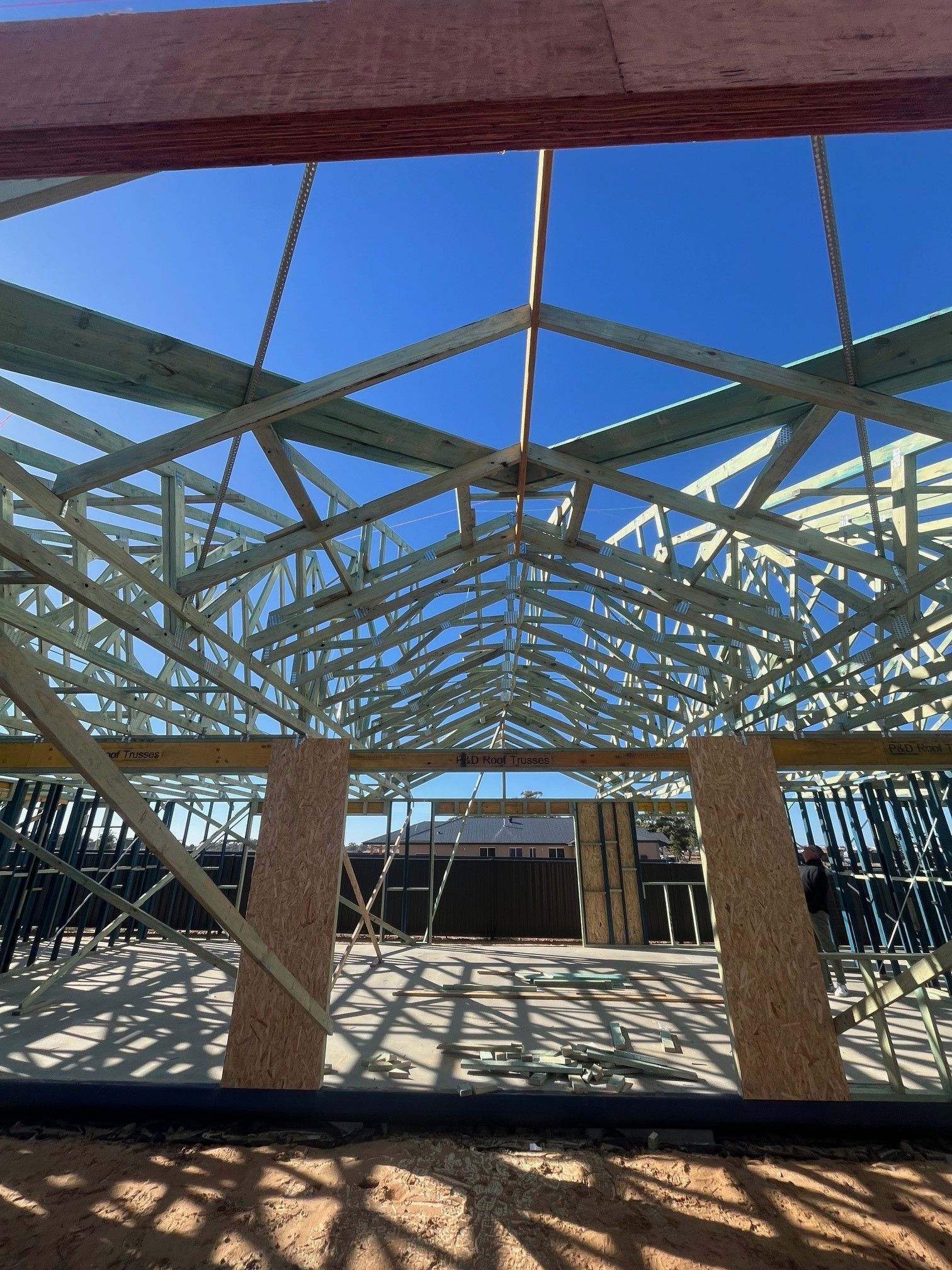 Wooden roof trusses under construction against a bright blue sky. Inside, light casts shadows on the floor.