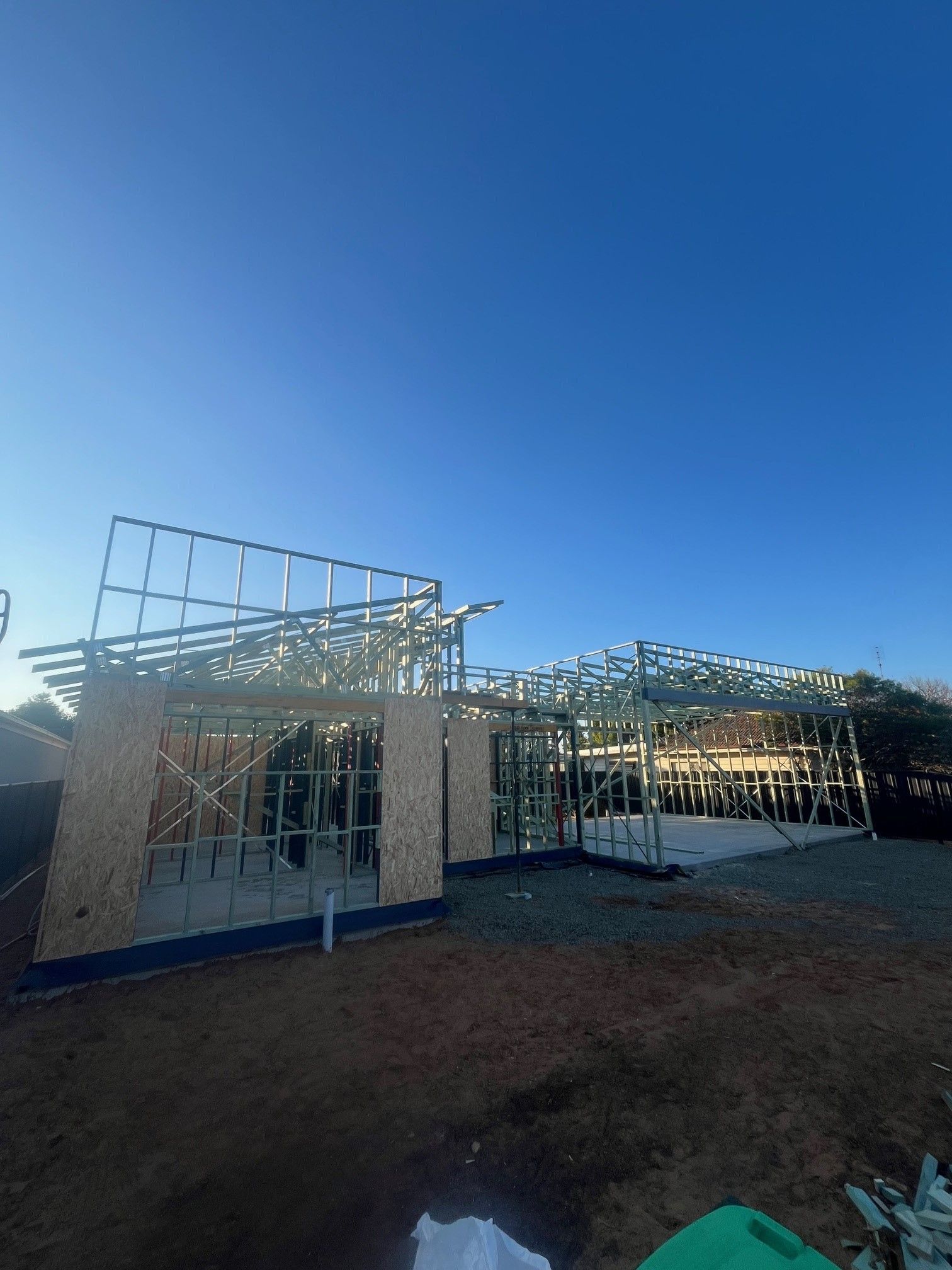 Metal frame of a house under construction on a clear, blue-sky day. Plywood sheathing is partially installed.