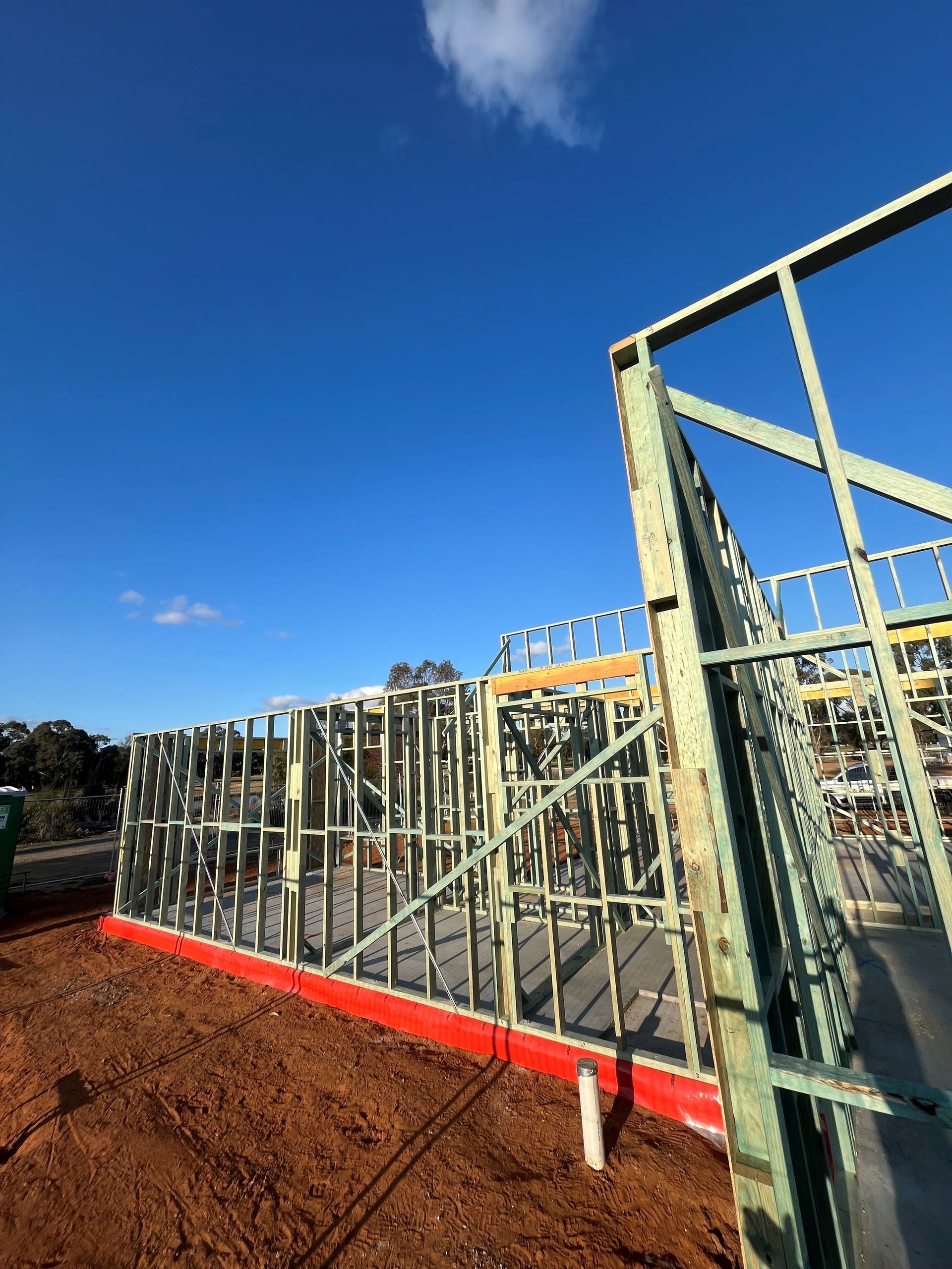 Construction site with exposed wooden frame. Walls and a roof are being built, a red barrier sits at the base.