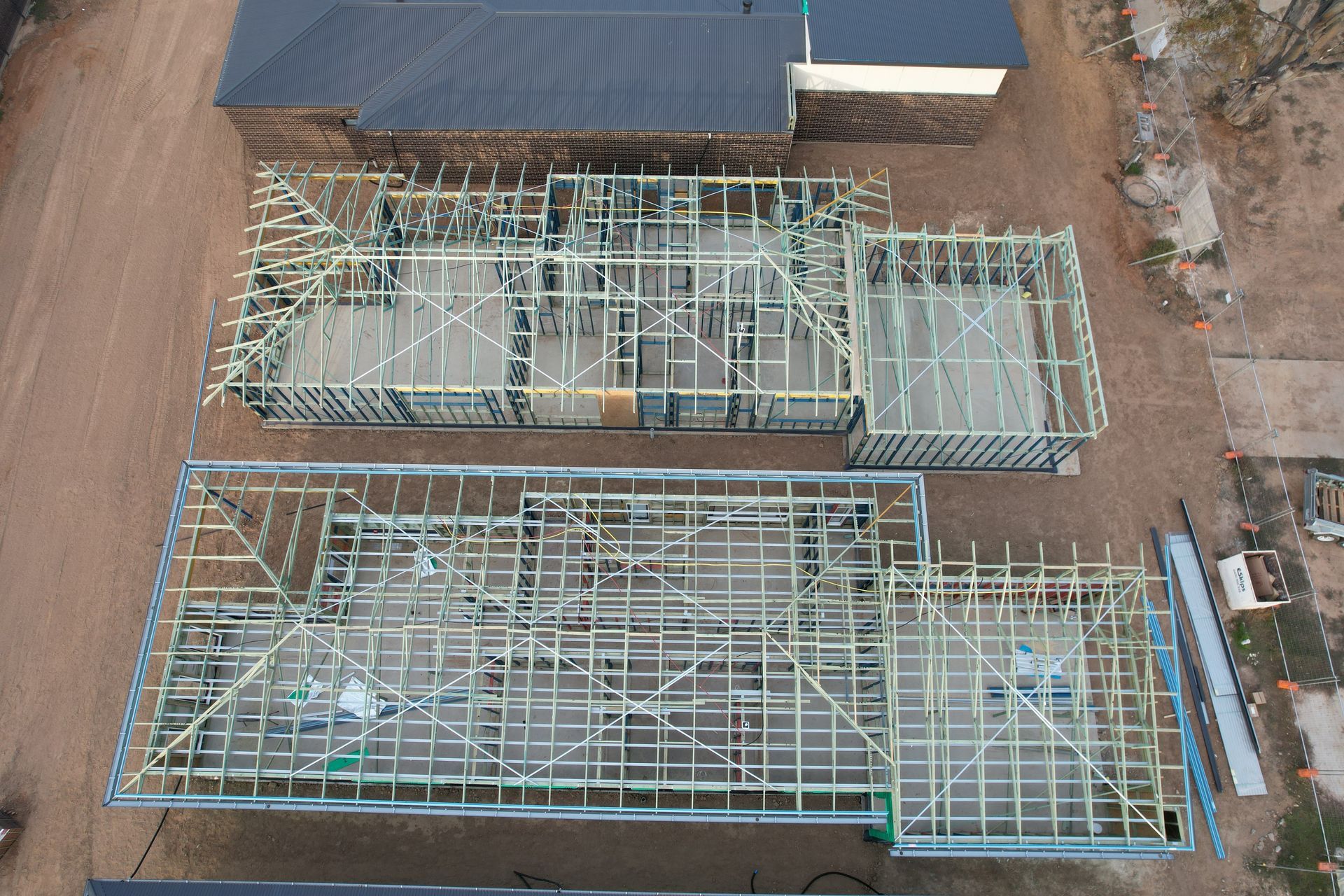 Overhead view of two house frames under construction; wooden beams outline the structures on a brown field.
