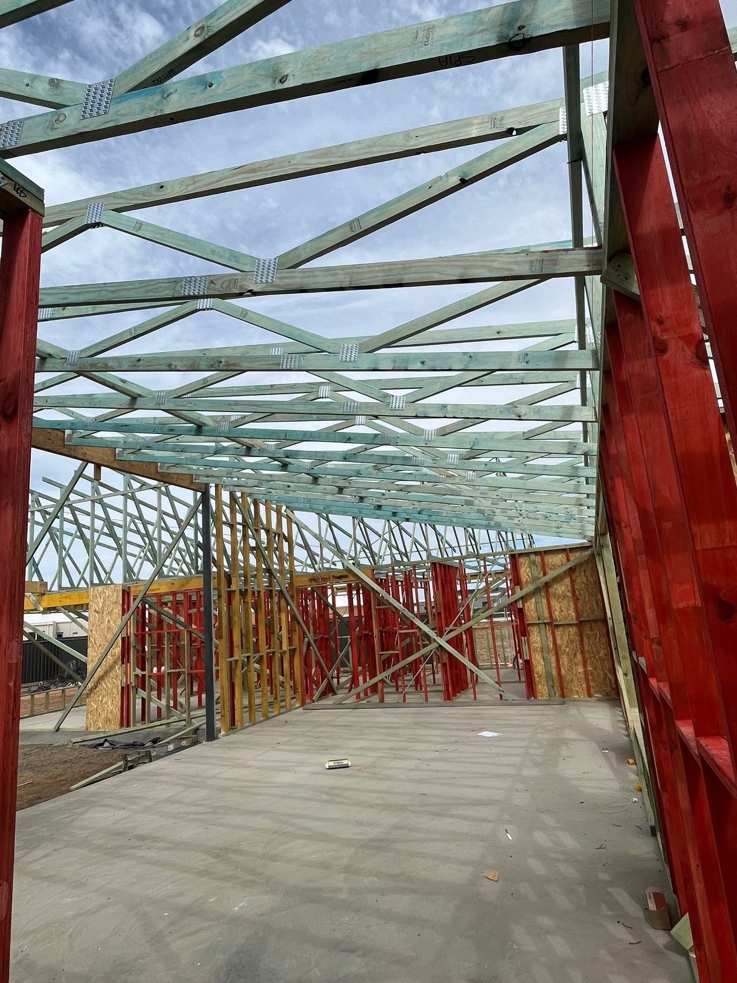Interior view of a building under construction with exposed wooden roof trusses and wall frames. 