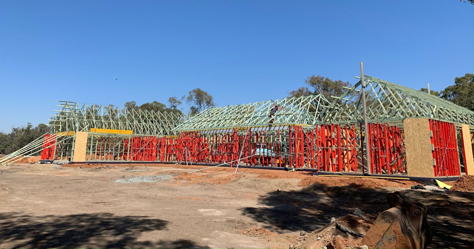 Construction site with a house frame being built; red formwork, wooden beams, and a blue sky.