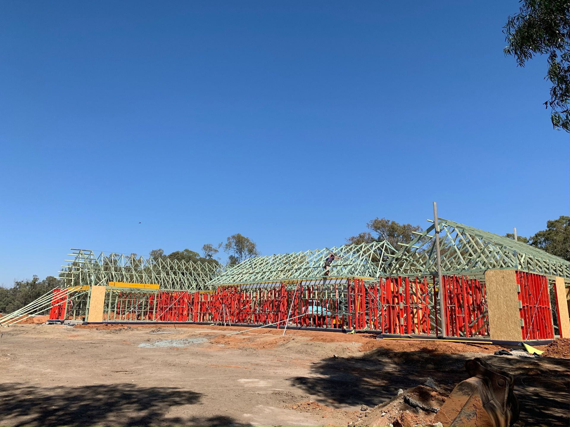 Construction site: Wooden frame of a building with red safety barriers, set against a clear blue sky.