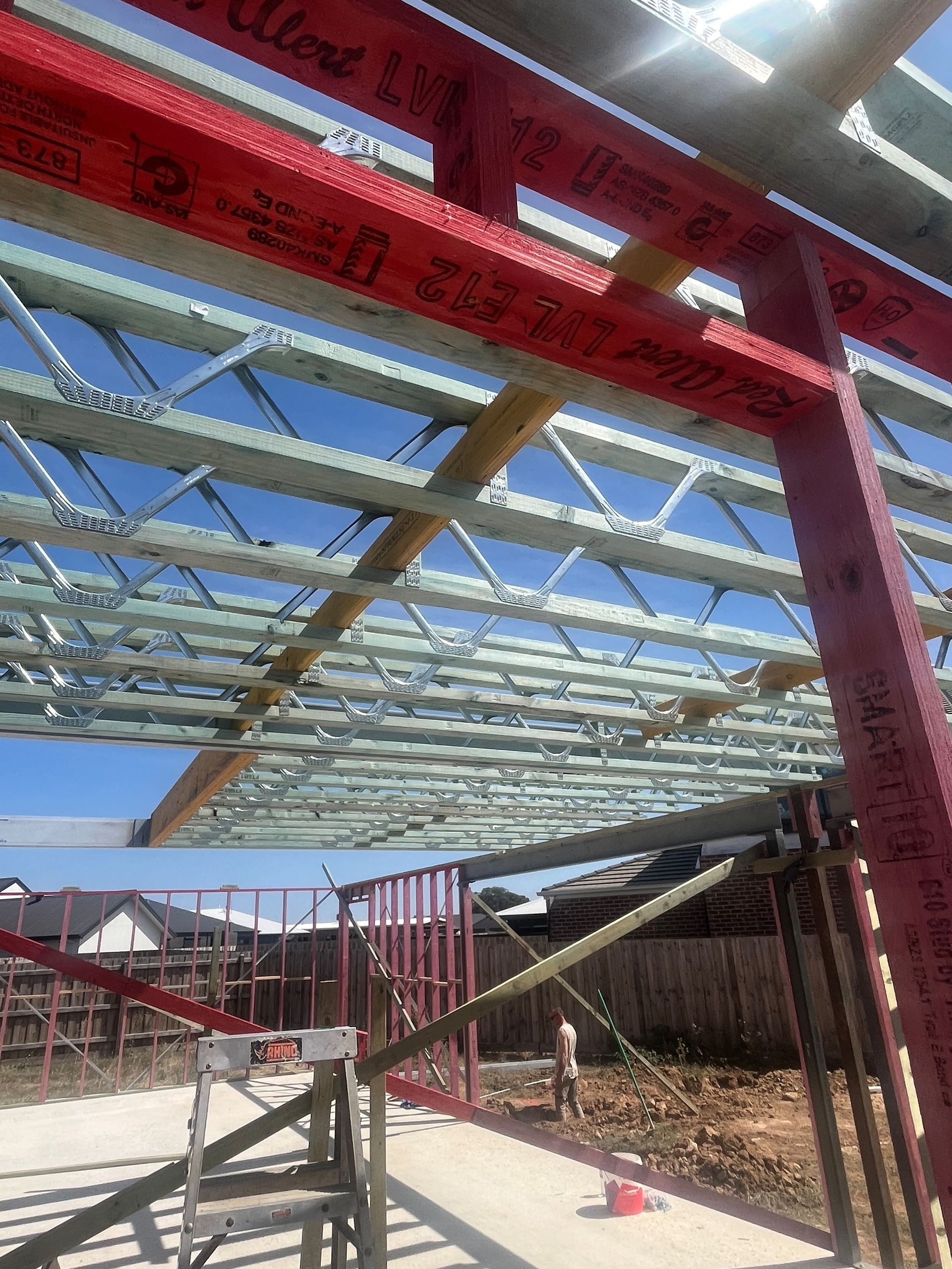 Construction site with red and metal beams forming a roof structure under a blue sky. 