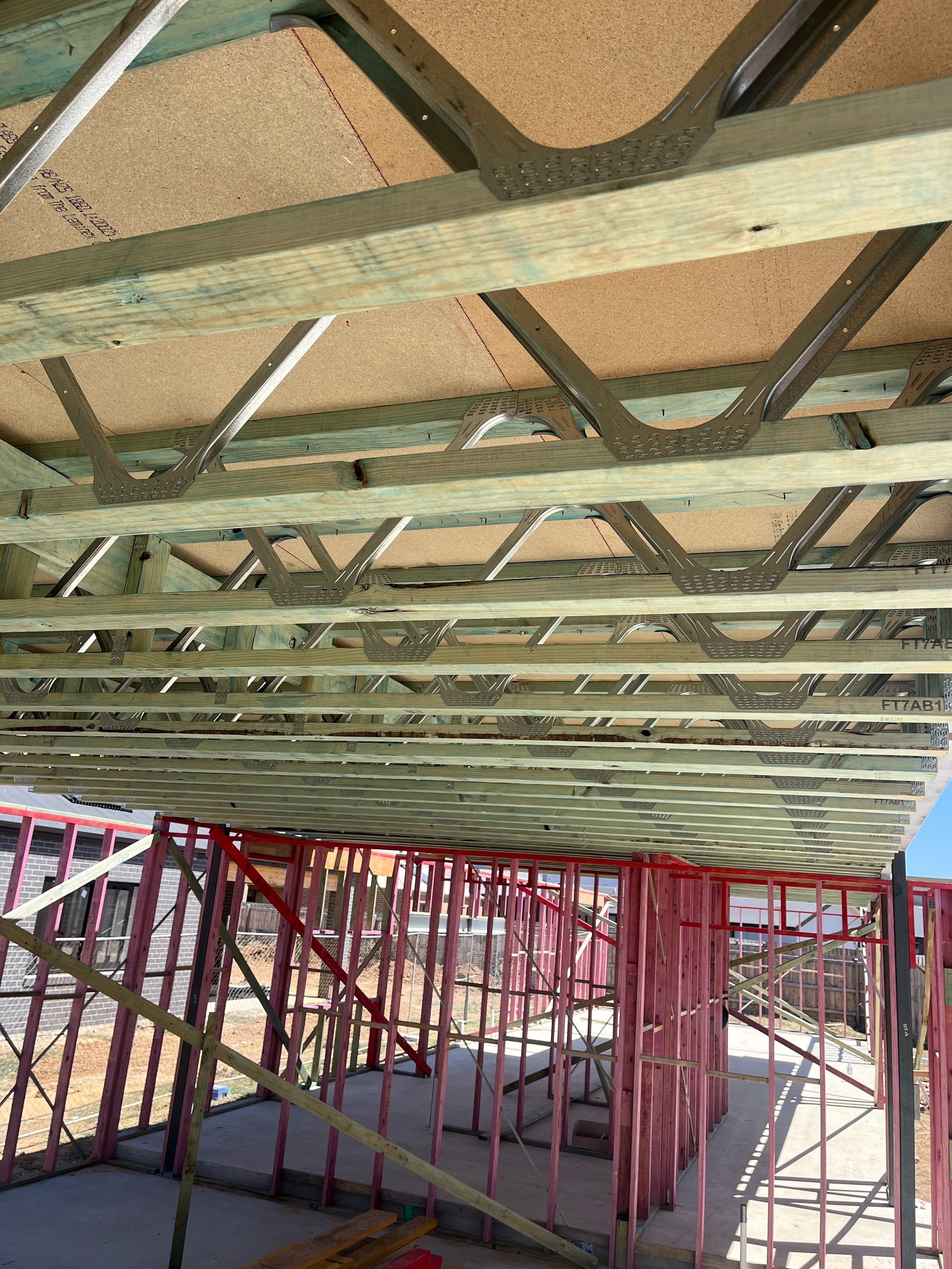 Wooden framework of a house under construction. Green joists support a particleboard ceiling over red-painted wall studs.