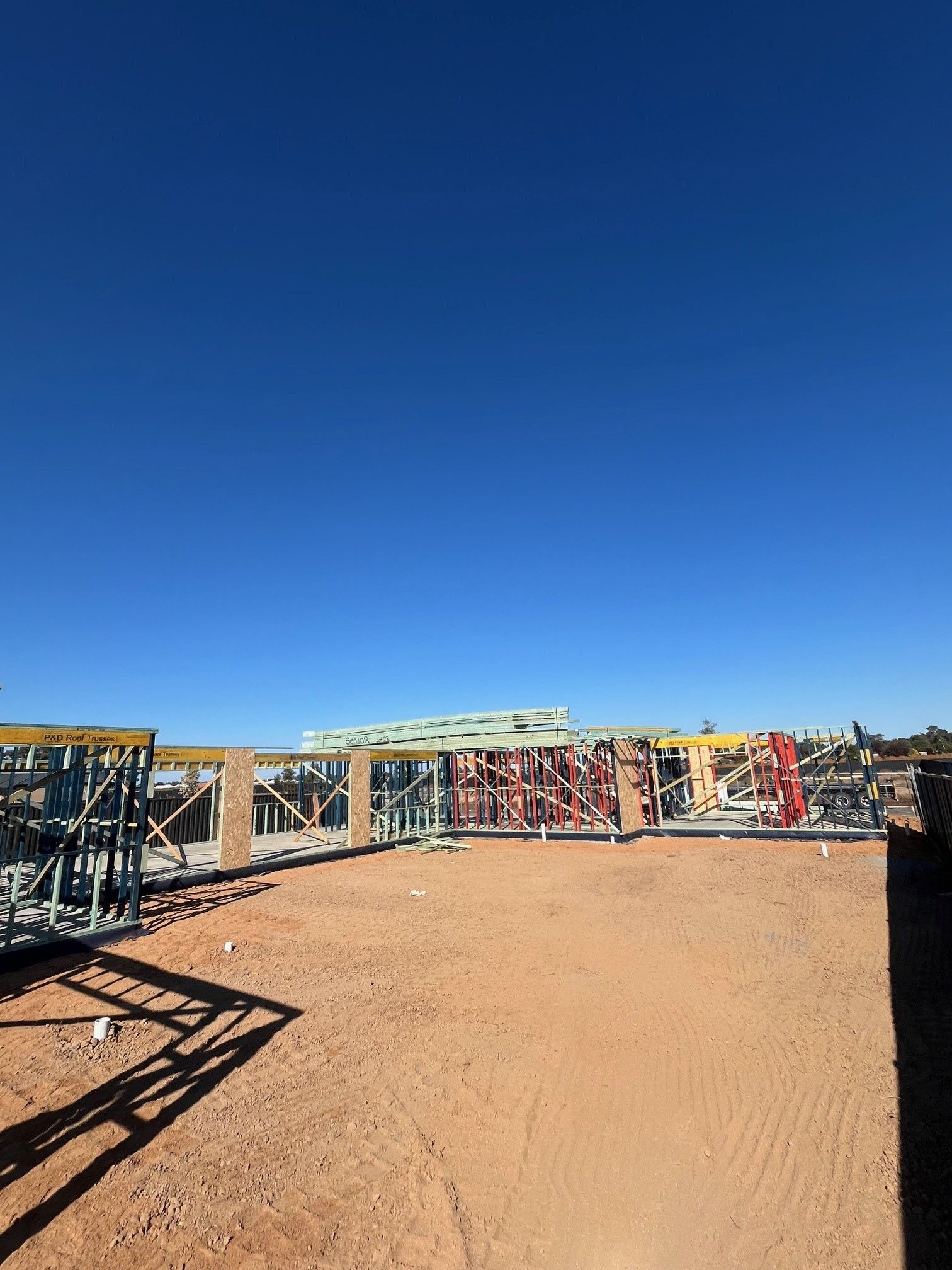 Construction site with blue sky. Steel frames and building materials on a dirt ground.